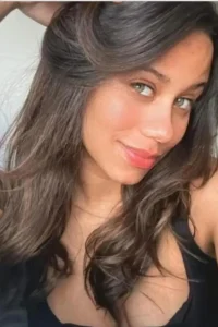 Milena in black satin bra and panties with a garter belt, arching gracefully on a velvet chaise.